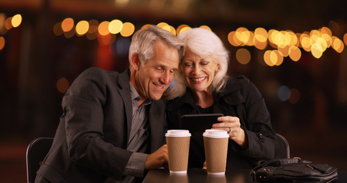 Older couple smiling while looking at cell phones. 
