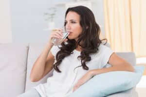 woman sitting on the couch while drinking a glass of water