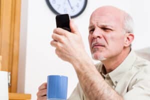 man sitting at table holding cup of coffee in one hand while holding cell phone close to his face 