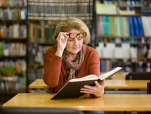Woman looking under her glasses at book